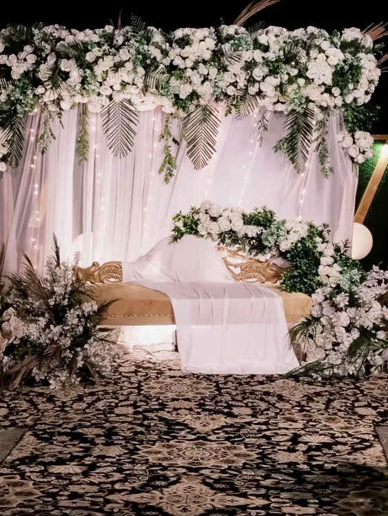 Blush draping and white flowers framing a white event sofa
