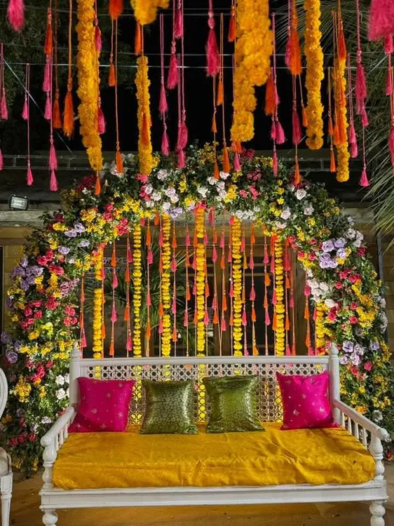 Colourful hanging floral strands above yellow seating with bright cushions